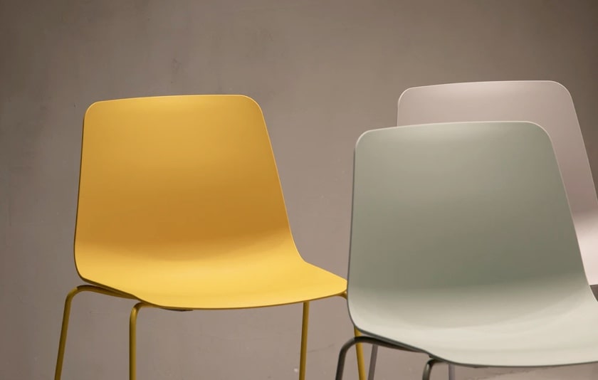 A yellow, a green and a pink chair in a cement colored room