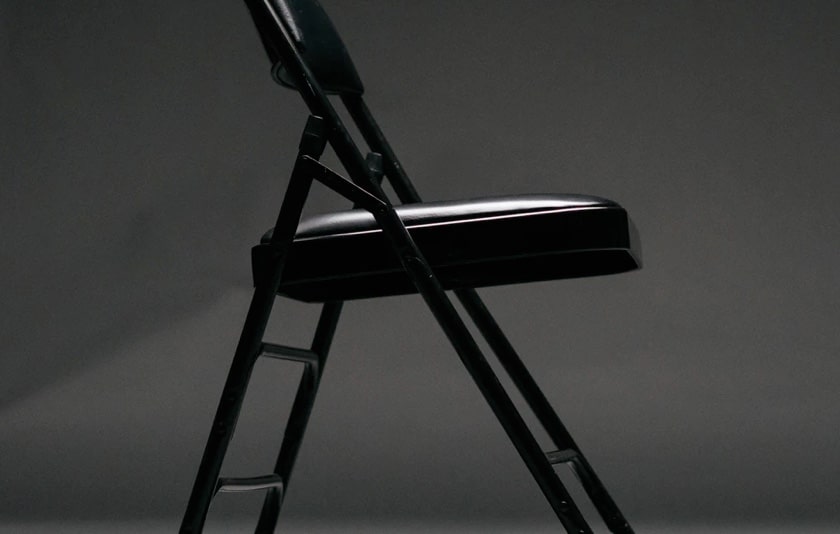A black and white image of a blach foldable chair with white light reflecting on it